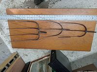 Three rusted vintage pitch fork ends laid side by side on wooden board with a metal ruler above for length measurement.