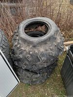 Stack of four black ATV tires with aggressive tread pattern, outdoors.