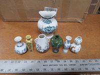 Top-down view showing all seven small Japanese porcelain vases in a line with measuring scale for size reference.