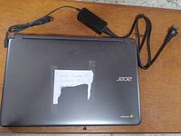 Closed Acer Chromebook laptop with power adapter on wooden surface.