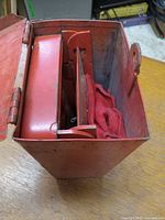 Red metal storage case with hinged lid containing the caution lenses and cloth covers