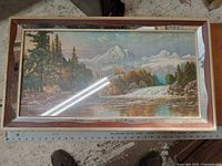 Full view of framed landscape picture showing deer by river with mountains and trees in background.