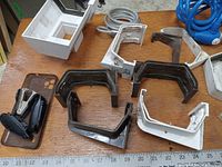 Eavestrough corner and end pieces and some miscellaneous metal hardware parts arranged on a wooden table.