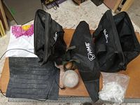 Photo showing three black tool bags including one Phillips brand, one HME crossbow bag, a rubber heating pad, a white baseball, and a plastic bag with white cable ties on a wooden surface.