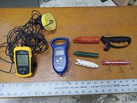 Overview of all fishing items laid out on a wooden surface including fish finder, scale, flashlight, lures, and tool