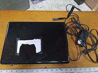 Top view of closed black HP laptop with charger cable coiled beside it on table with ruler.
