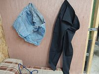 Photo showing light blue denim jean shorts and black dress pants hanging on a door.