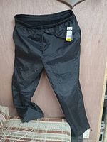 Front view of black/anthracite snow pants hanging on a wooden background showing elastic waistband and roomy legs.