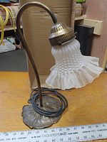 Side view of the lamp showing the curved metal stem, lily pad base, and ruffled hobnail pattern glass shade.