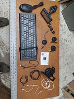 Full view of the electronics laid out on a wooden table including keyboard, mouse, cameras, mounts, cables, and white box device.