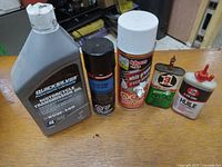 Photo showing five items including Quicksilver motorcycle transmission oil, Motomaster spray, Kleen-Flo white grease spray, and two 3-in-1 oil cans.
