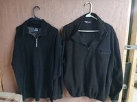 Two black men's sweaters hanging on hangers, showing full front views and highlighting quarter-length zippers and collar styles.