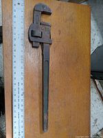 Full view of the 24 inch Stillson pipe wrench showing its length and condition on a wooden surface with a measuring ruler.