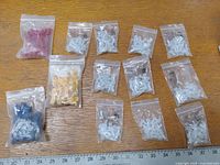 Multiple small bags with different colors and sizes of wire connector caps on wooden surface alongside a ruler for scale.