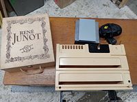 Wooden René Junot wine box closed with rope handle on table alongside HP storage device, paper towel holder, and black alarm clock