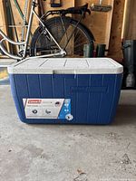 Front view of blue Coleman chest cooler with white lid, showing capacity label and brand logo.