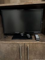 Samsung 23-inch flat screen TV placed on a brown cabinet with two remote controls beside it.