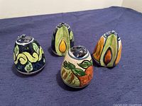 Four hand-painted Talavera salt and pepper shakers with intricate floral and geometric designs in blues, oranges, and greens placed on blue fabric.