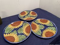 Three large hand-painted Talavera ceramic serving plates arranged on a dark blue cloth showing the sunflower design and overall size.
