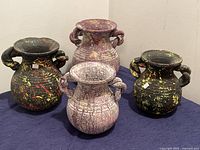 Set of 4 decorative Mexican painted clay vases arranged on a blue cloth showing size, shape, and color variations.