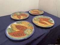 Four Talavera ceramic serving plates displayed on a dark cloth, showing colorful hand-painted fruit patterns.