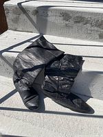 Photo showing one pair of black knee-high boots with slouchy design and wrinkled texture, positioned on concrete steps.