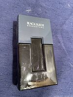 Closed bottle of Black Suede Essential perfume showing front with logo on gray cap and black glossy bottle body.