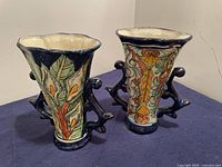 Two blue and terracotta Talavera ceramic vases with floral designs and double handles, side by side on blue fabric