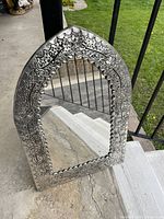 Full view of the elegant arch-shaped pressed tin mirror placed on concrete revealing its floral embossed border and detailed design.