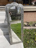 Full view of the full length mirror standing on concrete with lawn background showing the entire pressed tin frame and reflective glass surface.