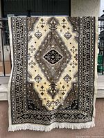 Full view of the rectangular area rug hanging, showing the overall geometric pattern, neutral color palette, and fringes on both ends.