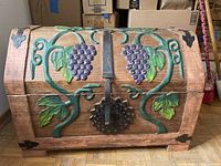 Front view of wooden chest showing hand-carved grapevine design, iron ring handle, and metal hinges.