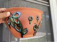 Photo of the front of the lamp showing terra-cotta clay with green glazed floral and leaf cutout design.