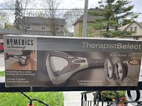 Box front showing the HoMedics TherapistSelect Wave Action Massager with mention of invigorating wave action and 4 custom massage attachments.
