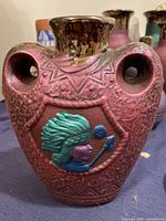 Front view of red textured painted clay serving jug, features turquoise and blue indigenous profile motif with two circular handles and glossy brown rim.