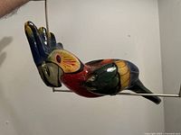 Side view of a multicolored papier maché hanging bird sculpture showing detailed painted feathers and beak on metal frame.