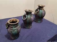 Front view of set of three hand painted clay hanging pots in turquoise and black with bronze rims.