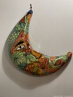 Front side of the crescent moon-shaped Talavera ceramic wall decor showing hand-painted colorful foliage and fruit motifs with signature hook for hanging.
