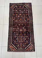 Full view of the rectangular dark blue Hamadan rug showing all over geometric and floral patterns with red, cream and green accents.