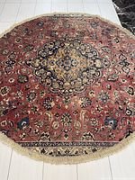 Full view of the round Persian Kashan rug showing central medallion and border design with red and blue floral patterns.