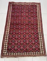 Full view of the rectangular red Tabriz rug with geometric and floral repeated pattern, beige borders and fringed edges, laid flat on tile floor.