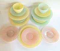 Top view of stacked pastel yellow, green, and turquoise ceramic dishware including cups, saucers, salad and dinner plates along with pink glass dessert plates in front.