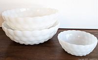 Four white Anchor Hocking bubble milk glass serving bowls, three larger and one small, stacked and displayed on wooden surface.