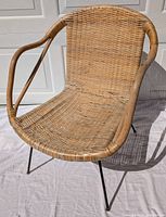 Front view of wicker chair showing natural woven seat and bentwood arms, black metal legs.