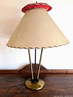 Full view of the atomic table lamp showing beige conical shade with red and natural fiber top detail and brass base with three rods.