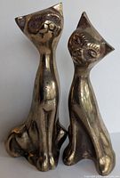 Front view of two brass cat figurines sitting side by side, showing facial details and body posture.