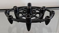 Front angled view of the black cast iron candle holder showing six taper candle slots and the circular spider web-like design in the middle.