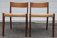 Front view of two Danish modern style dining chairs with teak wood frames and woven seats, displayed side by side.