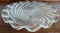 Clear round glass plate with a swirling tempest pattern visible from a tilted side angle, showing texture and wavy rim