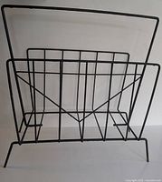 Front view of black metal wire magazine rack showing rectangular compartments and carrying handle.
